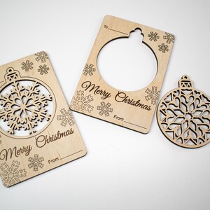 May include: Two wooden Christmas gift tags with a cut-out snowflake ornament. The tags have the text "Merry Christmas" and spaces for "To" and "From". A separate wooden snowflake ornament is also included.