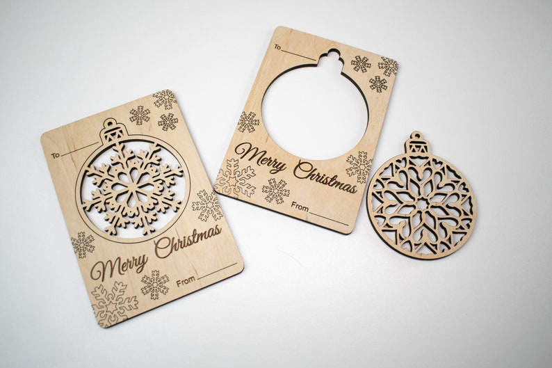 May include: Two wooden Christmas gift tags with a cut-out snowflake ornament. The tags have the text "Merry Christmas" and spaces for "To" and "From". A separate wooden snowflake ornament is also included.