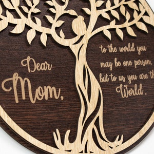 May include: A round wooden sign with a carved tree design and the words "Dear Mom, to the world you may be one person, but to us you are the World."