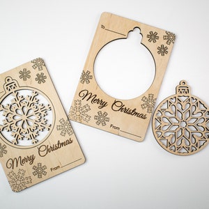 May include: Three wooden Christmas ornament gift tags with a snowflake design. The tags have a cut-out shape of an ornament and the words "Merry Christmas" and "To" and "From".