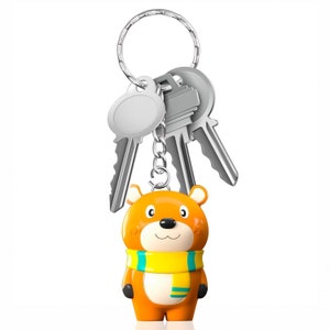 May include: A silver key chain with a small orange bear charm wearing a yellow and blue scarf. The bear has a friendly face with black eyes and a small black nose.