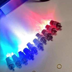 Op de afbeelding: Een verzameling kleine LED-lampjes in rood, blauw en helder. De lampjes zijn in een rij gerangschikt, met de rode lampjes rechts, blauw links en helder in het midden. De lampjes zijn aan en geven een heldere gloed af.