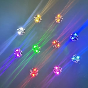 Puede incluir: Una taza de cerámica blanca con asa negra y el texto "But First, Coffee" en negrita negra. La taza se encuentra sobre un fondo borroso, sugiriendo un ambiente acogedor.