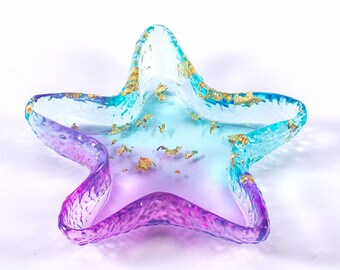 May include: A teal and purple resin starfish dish with gold flecks. The dish is perfect for holding jewelry, keys, or other small items.