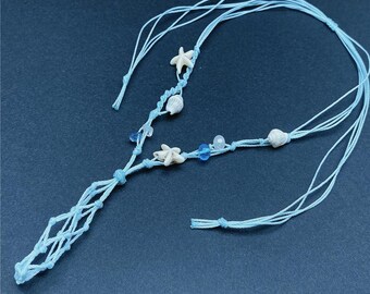 May include: A light blue macrame necklace featuring starfish, seashells, and blue beads. The necklace has a knotted design with multiple strands and a decorative macrame section. The background is a solid dark blue.