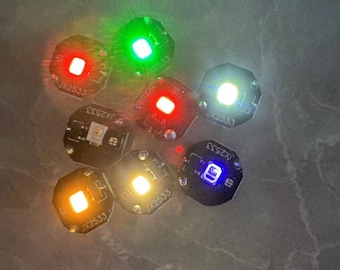 May include: A collection of small, round LED lights in various colors, including red, green, white, yellow, and blue. Each light is mounted on a small black circuit board with the text "JX2533" printed on it. The lights are arranged on a gray surface.