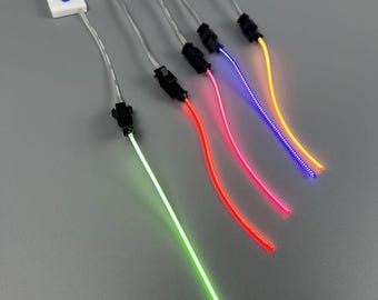 May include: Several fiber optic light strands with various colors, including green, red, pink, blue, and yellow. Each strand has a black connector and a white plastic base with a blue button. The strands are arranged diagonally against a gray background.