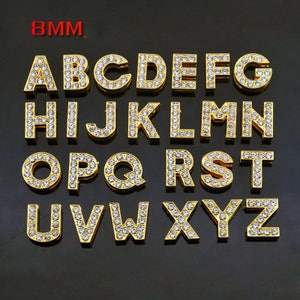 May include: A set of 26 gold-toned letter charms, each encrusted with clear rhinestones. The letters are arranged in alphabetical order, starting with A and ending with Z. The charms are 8mm in size.
