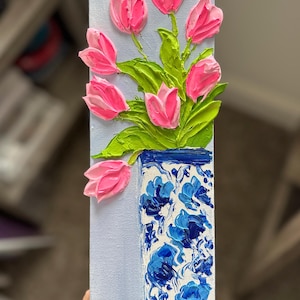 May include: A vertical painting of pink tulips in a blue and white vase. The tulips are textured and stand out from the light blue background. The vase has a floral pattern.