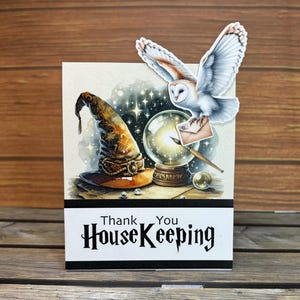May include: A greeting card with a wizard theme. The card features a wizard's hat, a crystal ball, and an owl carrying a letter. The text on the card reads "Thank You Housekeeping". The background has a starry night design.