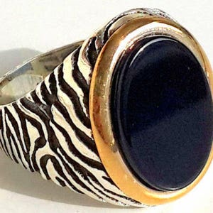 Peut inclure: Une bague en argent avec une pierre ovale noire sertie dans une bélière dorée. La bande de la bague est décorée d'un motif de rayures de zèbre.