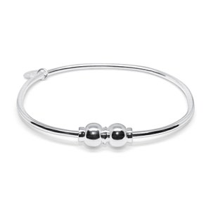 May include: A silver bangle bracelet with two round beads. The beads are connected by a thin metal bar.