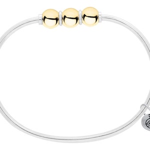 May include: A silver bangle bracelet with three gold beads and a small silver charm with a wave design.