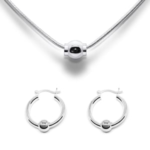 May include: A silver necklace with a round pendant and matching hoop earrings. The necklace and earrings feature a simple, elegant design.