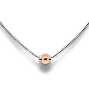 May include: A silver necklace with a polished rose gold bead pendant. The pendant is a sphere, and the chain has a snake-like design. The necklace is displayed on a white background.