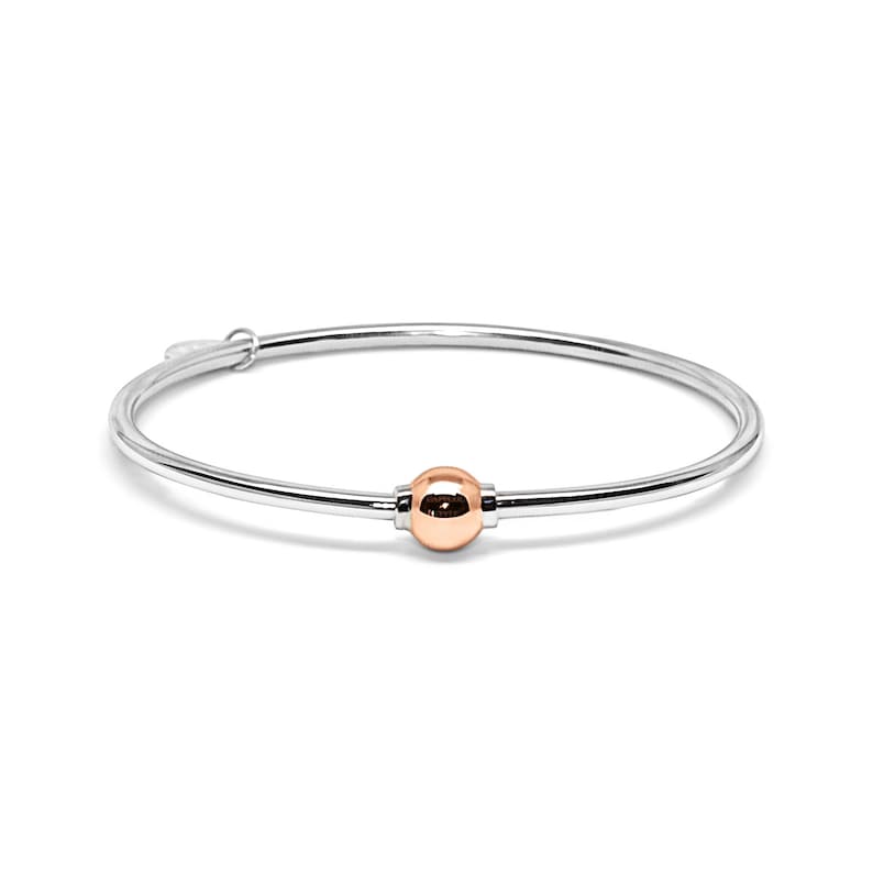 May include: A silver bangle bracelet with a single rose gold bead.