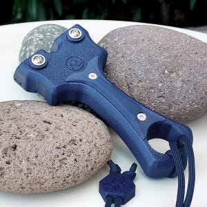 May include: A dark blue 3D-printed catapult featuring a textured surface, three silver-toned metal screws, and a circular handle base. A matching dark blue hexagonal bead is attached to the handle with a dark blue cord, showcasing a star emblem.