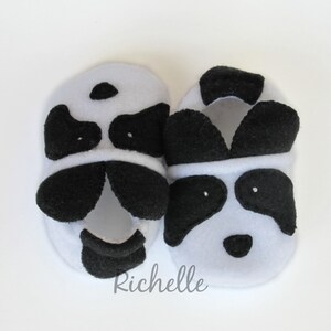 May include: A pair of black and white panda baby booties. The booties are made of soft fleece and have a black nose and eyes.