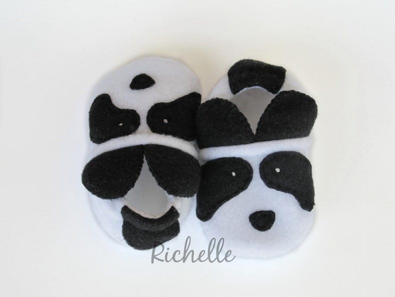 May include: A pair of black and white panda baby booties. The booties are made of soft fleece and have a black nose and eyes.