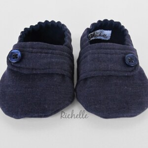 May include: A pair of navy blue baby booties with a button closure and a label that says "Richelle".