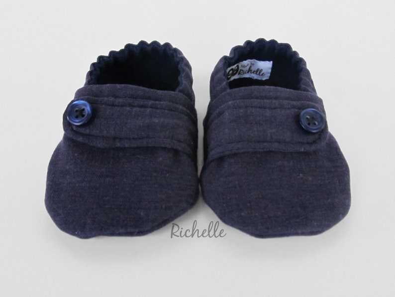 May include: A pair of navy blue baby booties with a button closure and a label that says "Richelle".