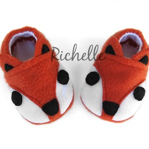 May include: A pair of orange and white fox-shaped baby booties with black felt accents.