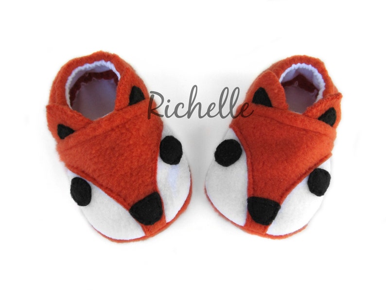 May include: A pair of orange and white fox-shaped baby booties with black felt accents.