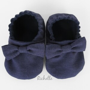 May include: A pair of navy blue baby shoes with a bow on the front.