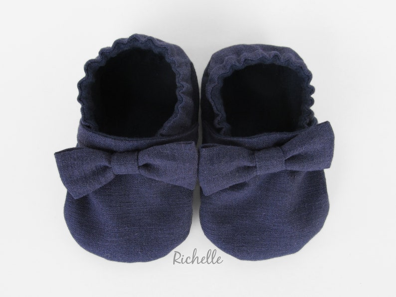 May include: A pair of navy blue baby shoes with a bow on the front.