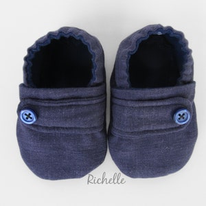 May include: A pair of dark blue baby booties with a button closure. The booties are made of a soft, textured fabric.