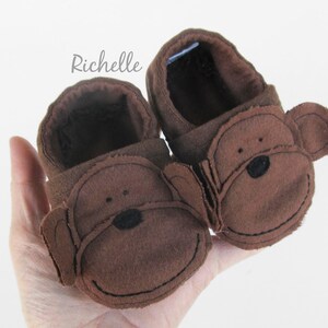 May include: A pair of brown baby booties with monkey faces. The booties have brown felt ears and black eyes and noses.