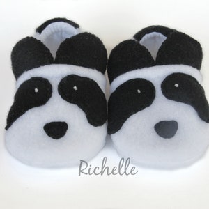 May include: A pair of white and black panda baby booties. The booties are made of soft fleece and have black felt eyes, nose, and ears.