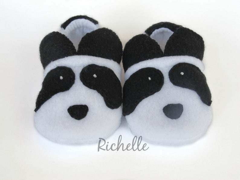 May include: A pair of white and black panda baby booties. The booties are made of soft fleece and have black felt eyes, nose, and ears.