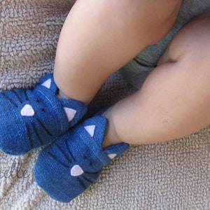 May include: A pair of blue denim baby booties with white cat ears and black whiskers.
