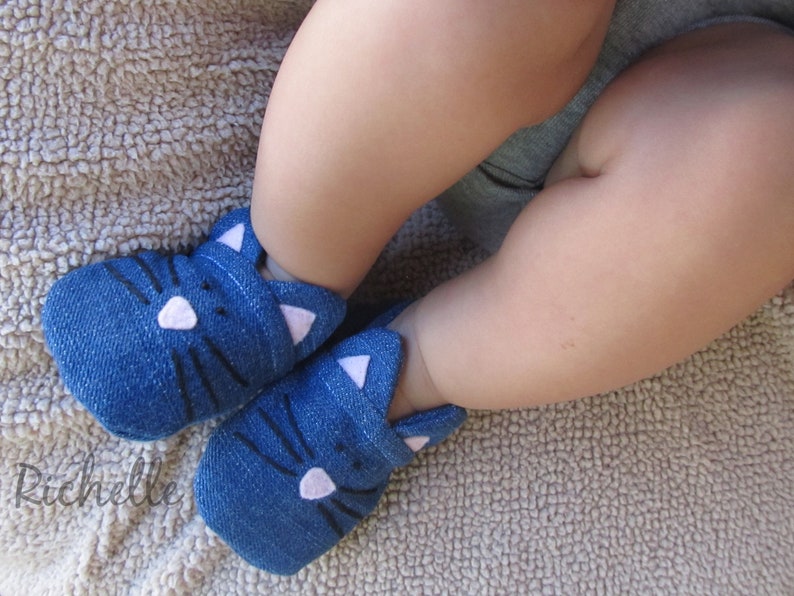 May include: A pair of blue denim baby booties with white cat ears and black whiskers.