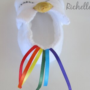 May include: White fabric unicorn slipper with a yellow horn and a rainbow of satin ribbon tails.