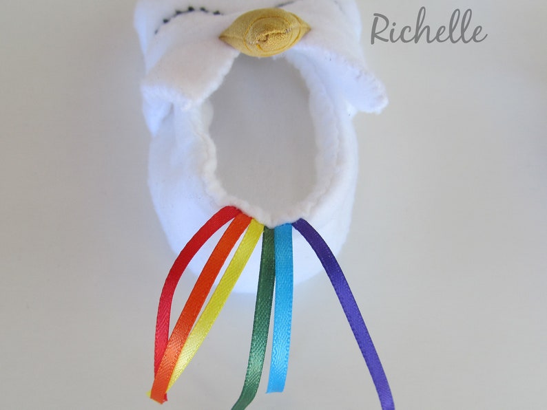 May include: White fabric unicorn slipper with a yellow horn and a rainbow of satin ribbon tails.