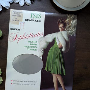Pode incluir: Caixa vintage de meias de nylon transparentes ISIS Seamless em Grey Vapor. A caixa apresenta uma imagem retro de uma mulher com um vestido verde e uma estola de pele branca. O texto "Sophisticates" e "Ultra High Fashion Tones" também está presente.