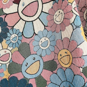 May include: A close-up of a colourful fabric with a repeating pattern of smiling flower designs. The flowers are in shades of blue, pink, yellow, and white.