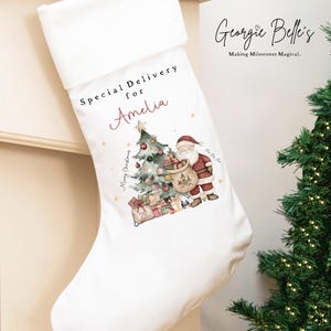 May include: White Christmas stocking with a folded cuff. It features a festive illustration of Santa Claus, a decorated Christmas tree, and gifts. The text "Special Delivery for Amelia" is printed on the stocking.