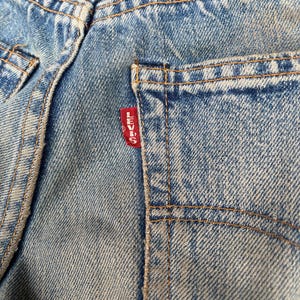May include: Light blue denim jeans featuring a classic five-pocket construction with visible orange contrast stitching. A small red fabric tab with the white text Levi's is sewn into the edge of the back pocket, highlighting the brand identity.