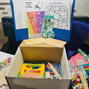 May include: A craft kit with a variety of supplies, including Crayola markers, paint, stickers, and coloring pages. The kit includes a Halloween word scramble and a color-by-number activity. A wooden cloud-shaped cutout is also included.