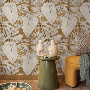 May include: A room with a botanical theme featuring a mustard-colored wallpaper with large white and gray leaves. A green side table holds decorative items. A woven basket with gourds sits on the floor, and a yellow ottoman is in the background.