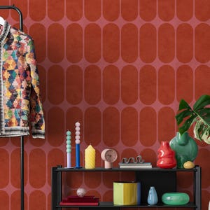 May include: A vibrant, patterned jacket hangs on a black coat stand. A black shelf displays decorative items like candles, vases, and a clock. The background features a red and pink oval pattern.