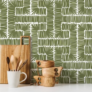 Puede incluir: Una tabla de cortar de madera, una taza blanca con utensilios de madera y tres tazas de madera se exhiben sobre un fondo geométrico blanco y verde oliva. Los artículos están dispuestos sobre una superficie blanca.