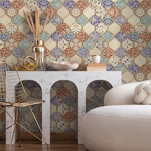 May include: A white marble console table with two arched openings, featuring a gold metal chair and a white ottoman. The table is decorated with a vase of dried reeds, a bowl of decorative white spheres, and a stack of books. The wall behind the table is covered in a patterned wallpaper with a geometric design in shades of blue, red, and gold.
