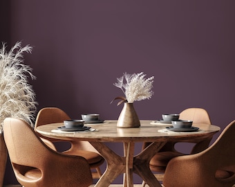 Op de afbeelding: Een eethoek met een ronde houten tafel en vier bruine stoelen. De tafel is gedekt met borden en kommen. Een vaas met gedroogde bloemen staat in het midden. De achtergrond is een effen paarse muur.