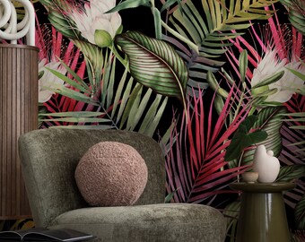 Op de afbeelding: Een pluche, rond, lichtbruin kussen ligt op een donkergroene fauteuil voor een zwarte achtergrond met een tropisch bladmotief. De bladeren zijn geschilderd in tinten groen, rood en wit.