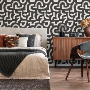 May include: A bedroom with a bed featuring a white and black patterned headboard, a brown wooden dresser, a grey chair, and a black and white patterned wallpaper.