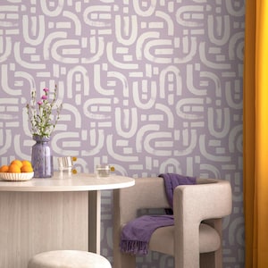 May include: A room with a lilac-colored wall featuring a white abstract pattern. A round table holds a vase of flowers and a bowl of oranges. A chair with a purple throw and a yellow curtain are also visible.